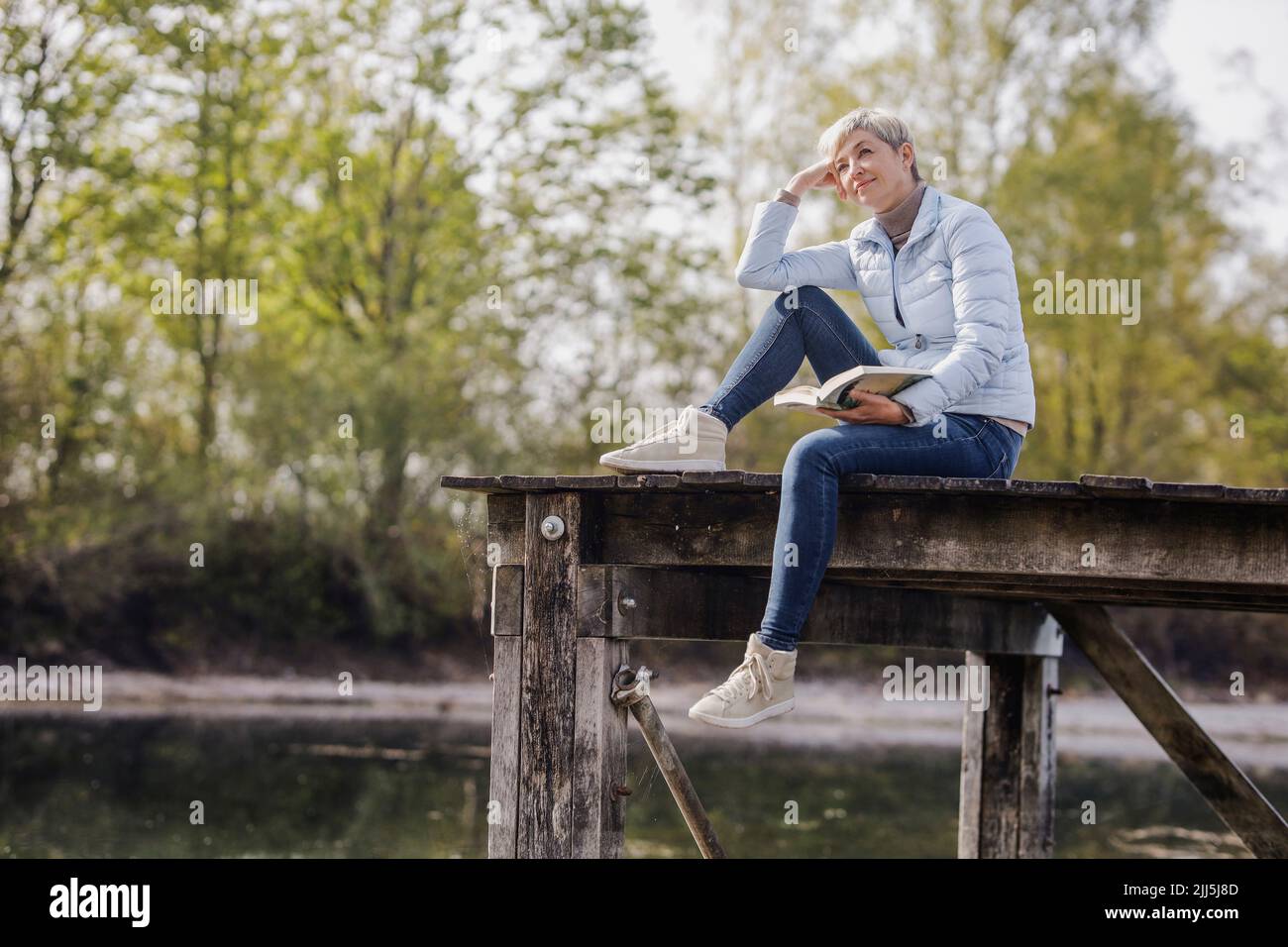Contemplative woman siting with book on pier Stock Photo
