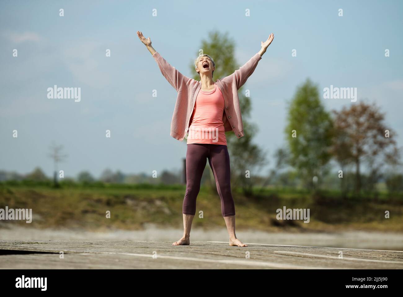 Mature woman standing with arms raised screaming on pier Stock Photo
