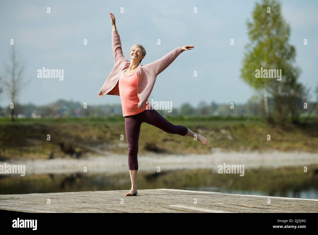 Happy woman with arms raised dancing on pier Stock Photo