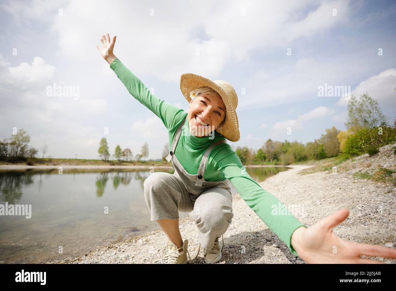 Cheerful mature woman with arms outstretched enjoying sunny day by lake Stock Photo