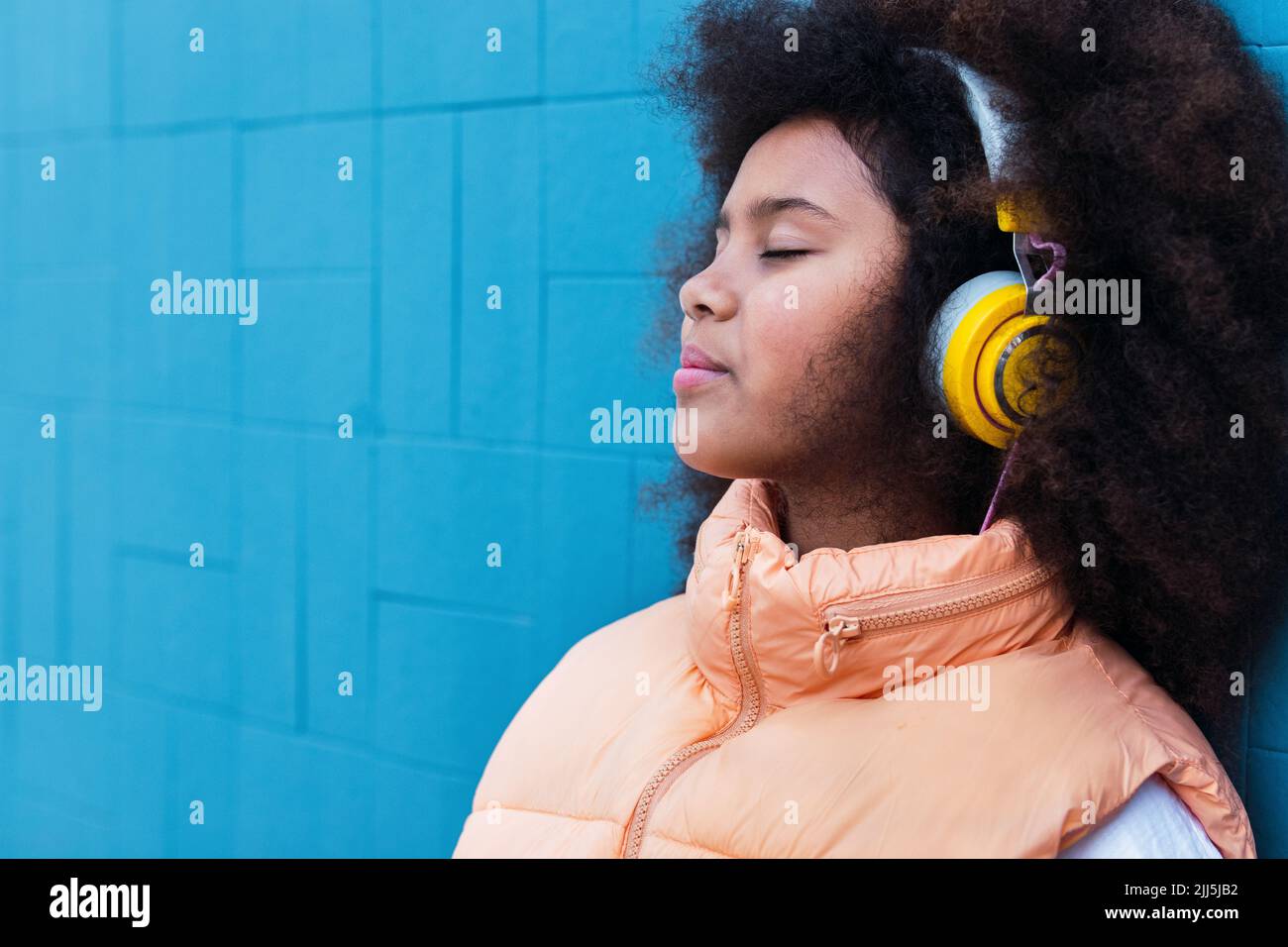 Girl with eyes closed listening music leaning on blue wall Stock Photo
