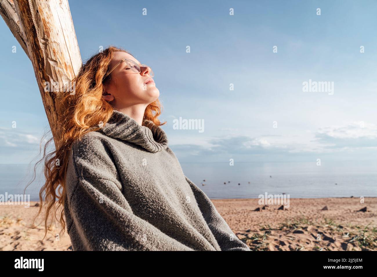 Woman enjoying sunlight leaning on tree at beach Stock Photo