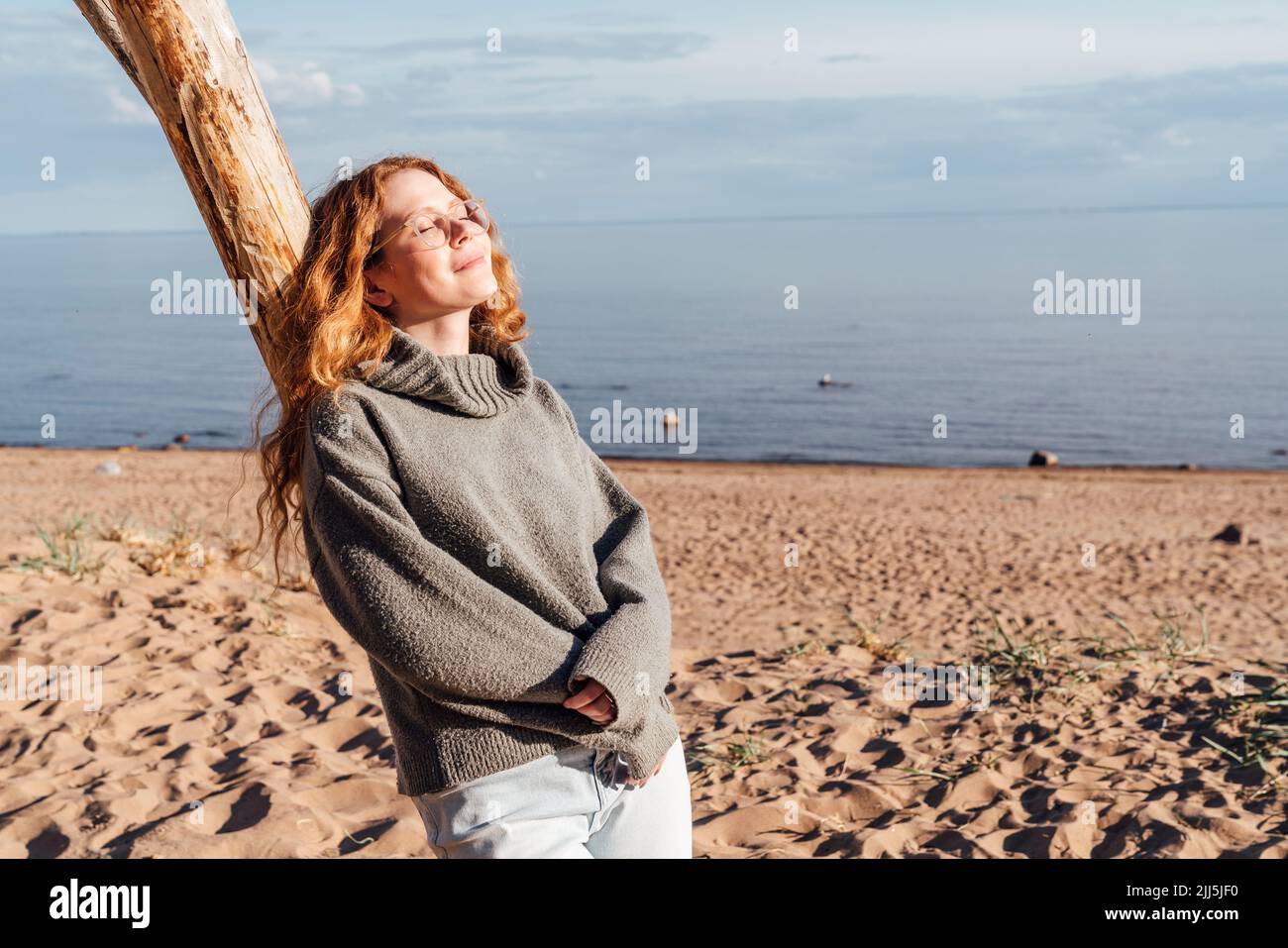 Young woman enjoying sunlight leaning on tree at beach Stock Photo