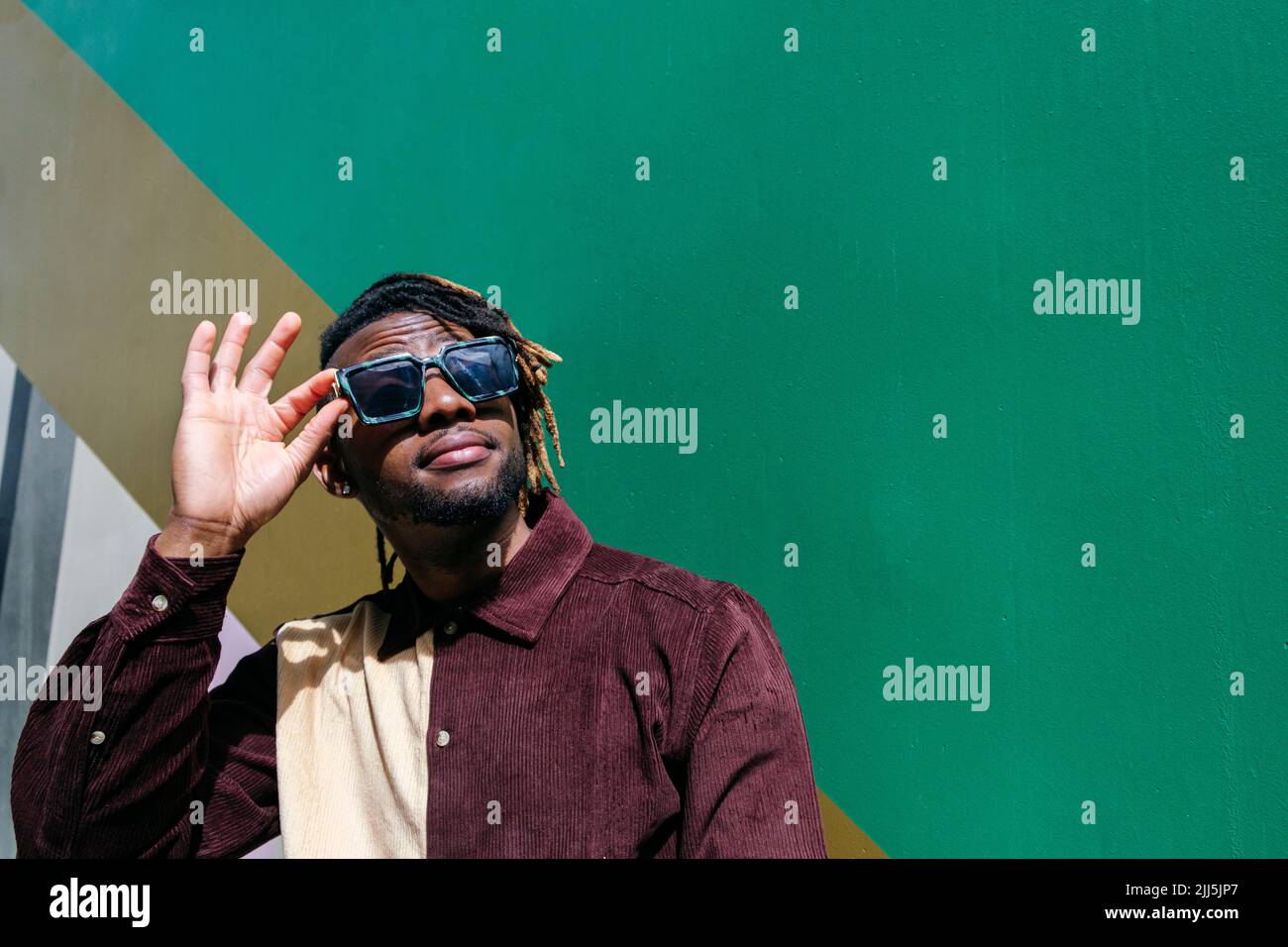 Man looking up wearing sunglasses by green wall Stock Photo