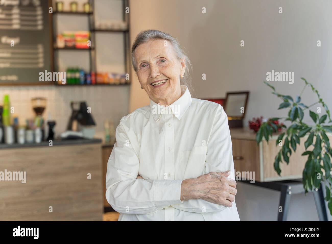 Happy senior woman with arms crossed standing in cafe Stock Photo
