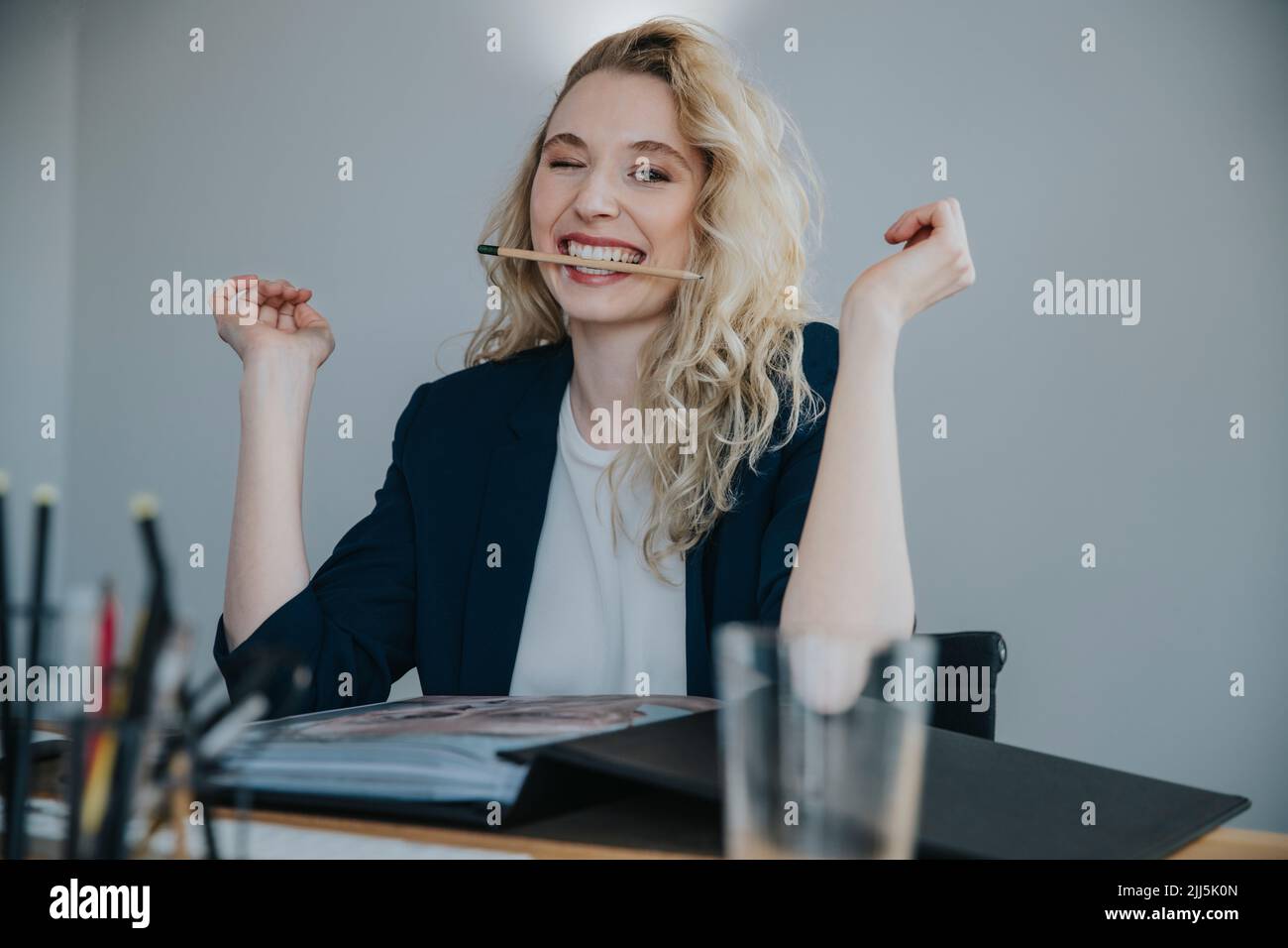 Young businesswoman holding pencil in mouth sitting at desk Stock Photo ...