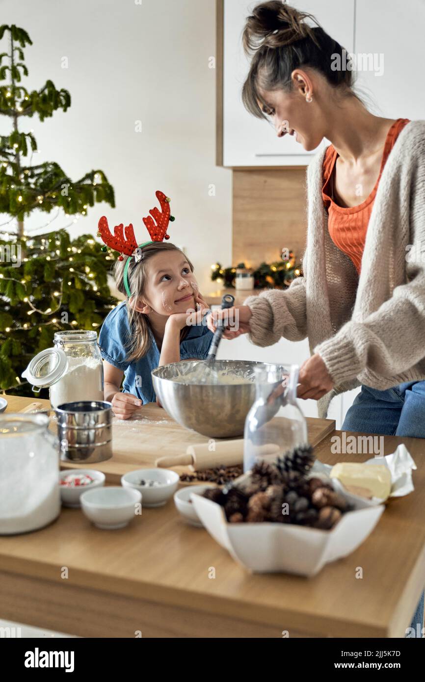 Smiling girl looking at mother mixing cookie dough in kitchen Stock Photo