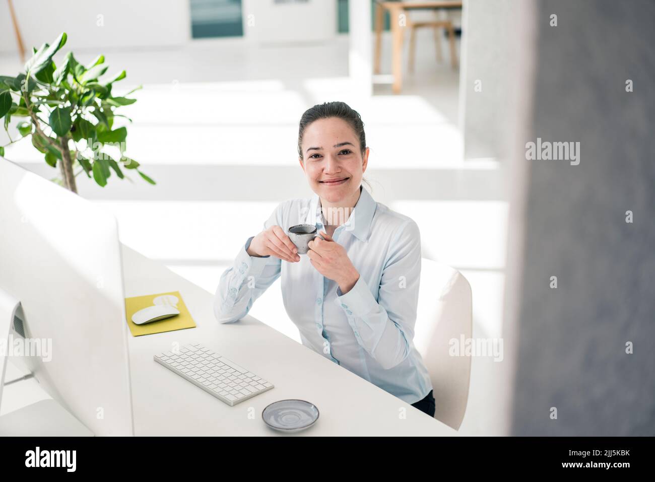 Smiling businesswoman with coffee cup at desk in office Stock Photo