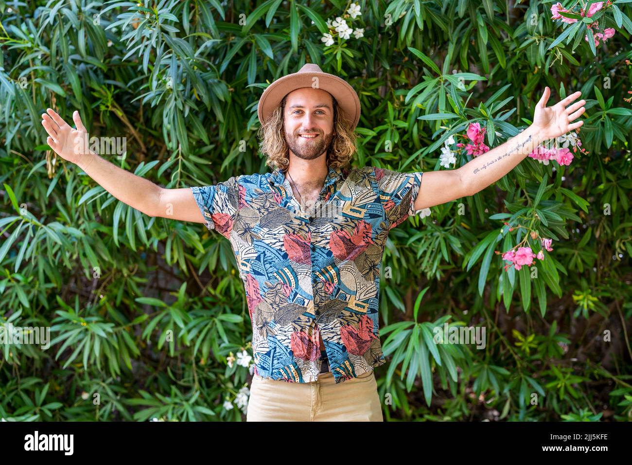 Smiling man standing with arms outstretched in front of plant Stock Photo