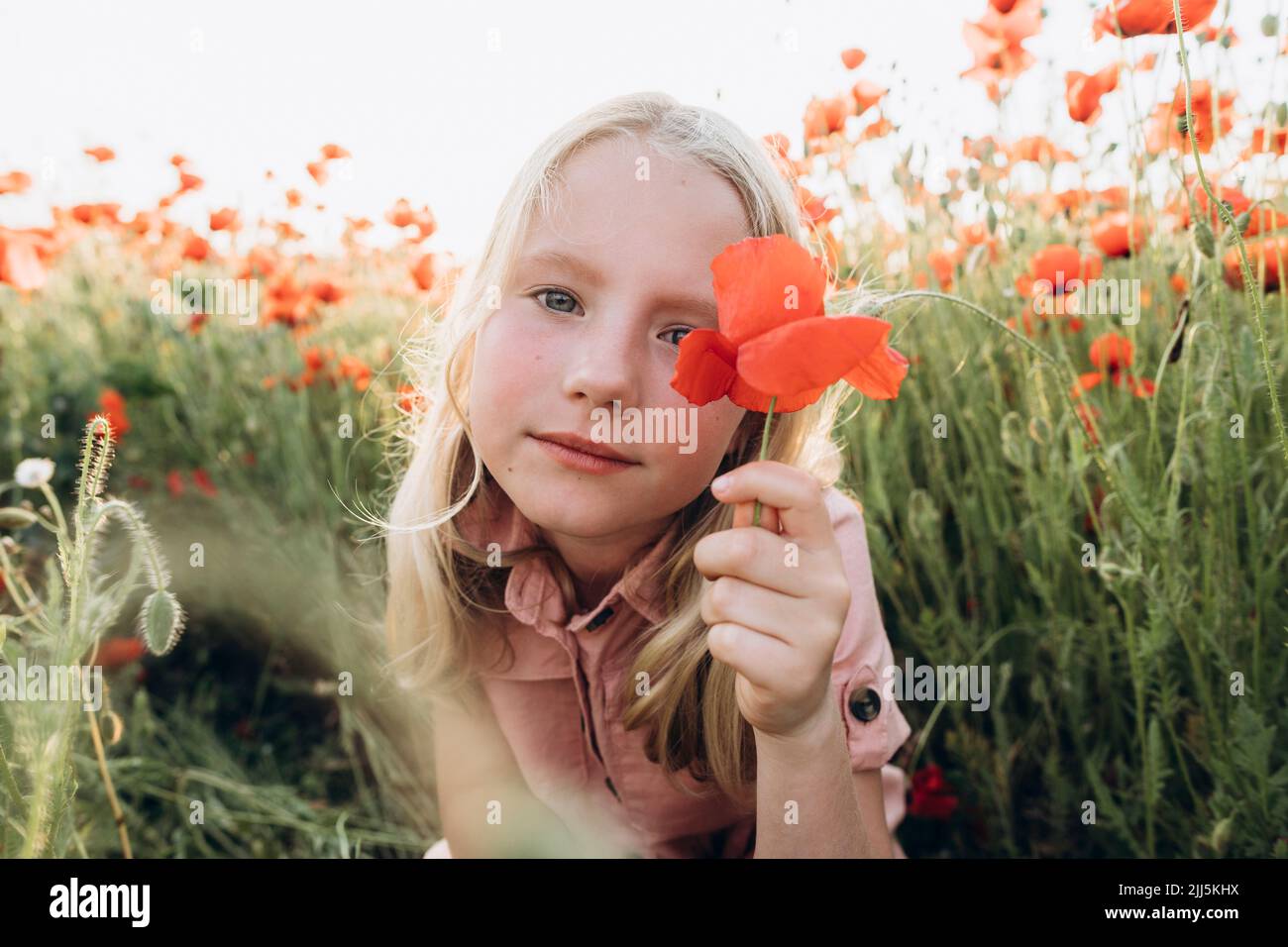 Blond girl holding red flower in poppy field Stock Photo