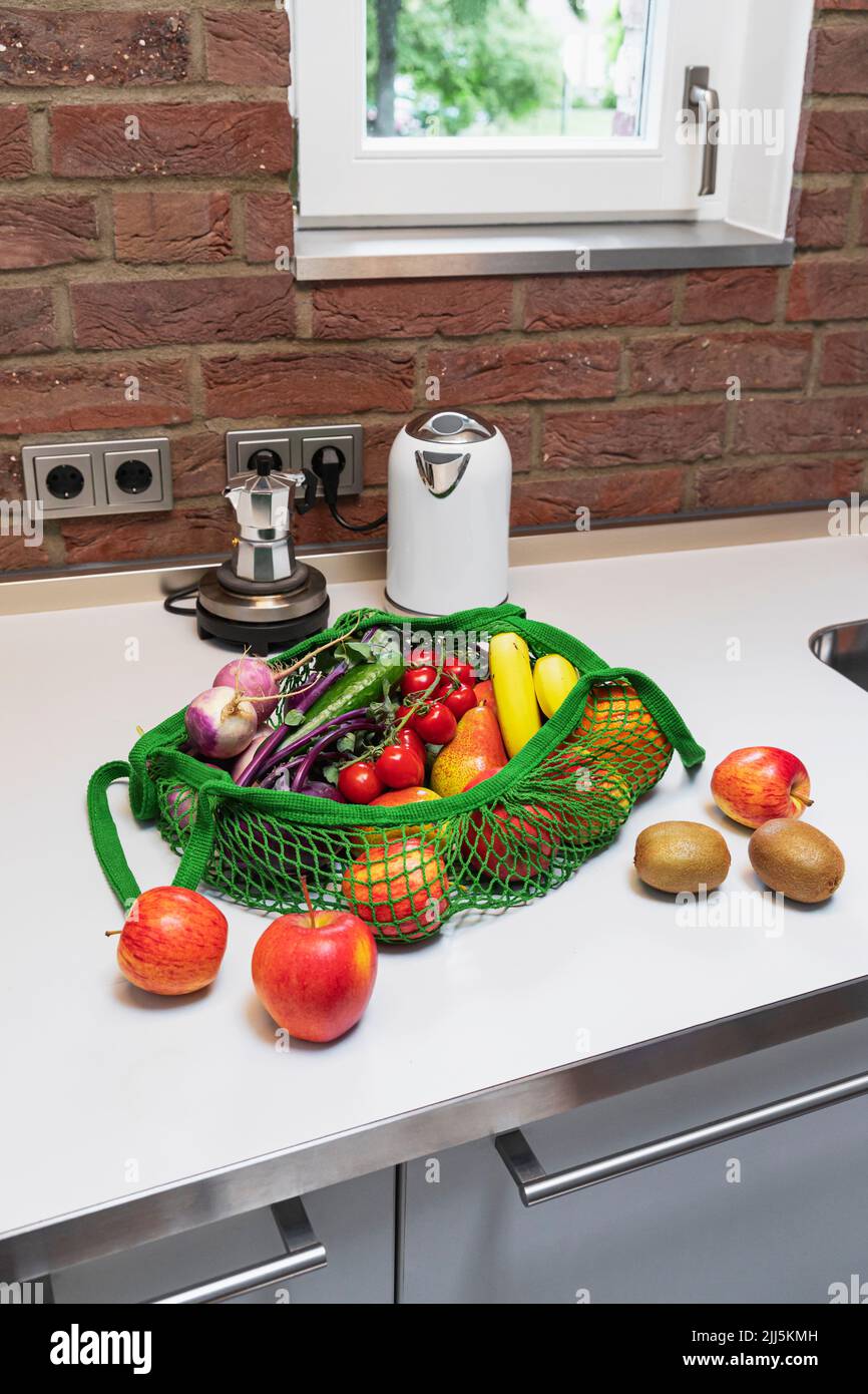 Fresh fruits and vegetables in reusable shopping bag on kitchen counter at home Stock Photo