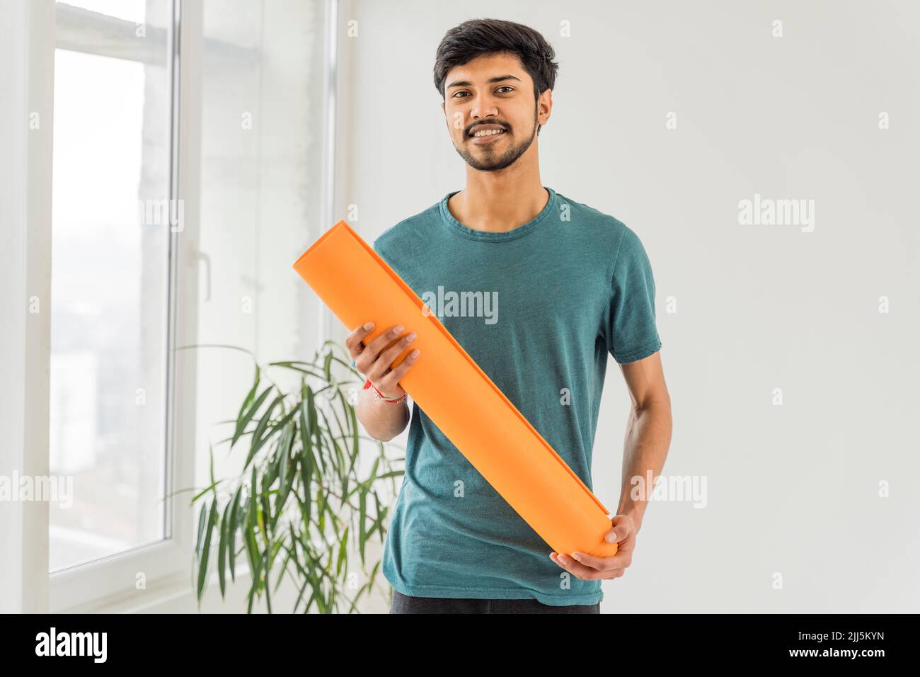 Smiling young man holding exercise mat in yoga studio Stock Photo