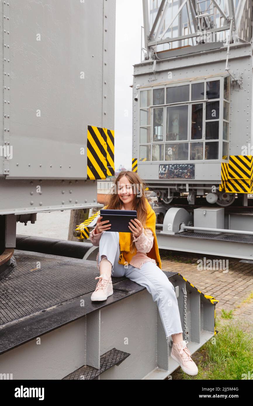 Happy young woman using tablet PC on museum harbor crane Stock Photo
