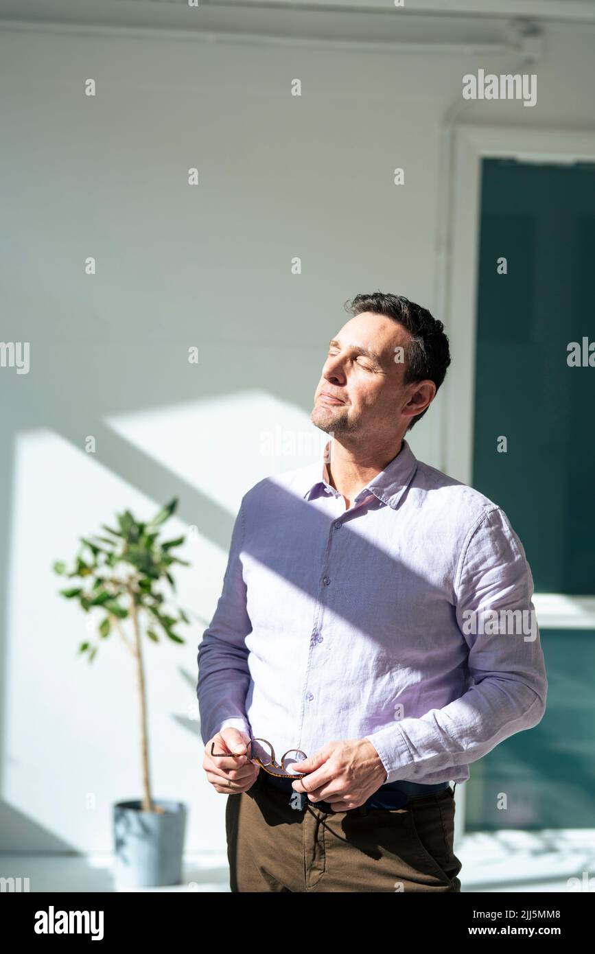 Businessman with eyes closed sunbathing at office Stock Photo
