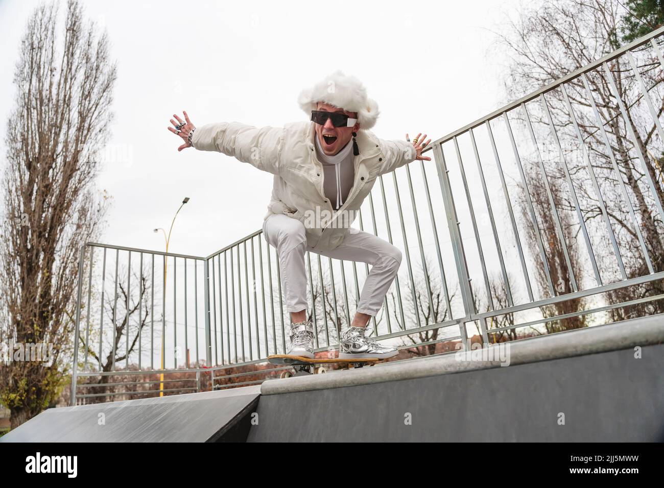 Happy man with mouth open balancing on skateboard by railing Stock