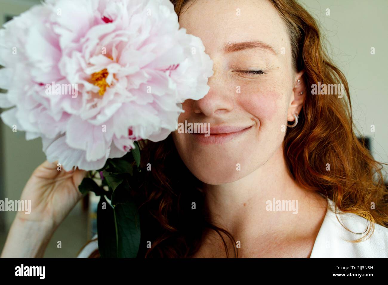 Woman with eyes closed holding pink flower in front of eye Stock Photo ...