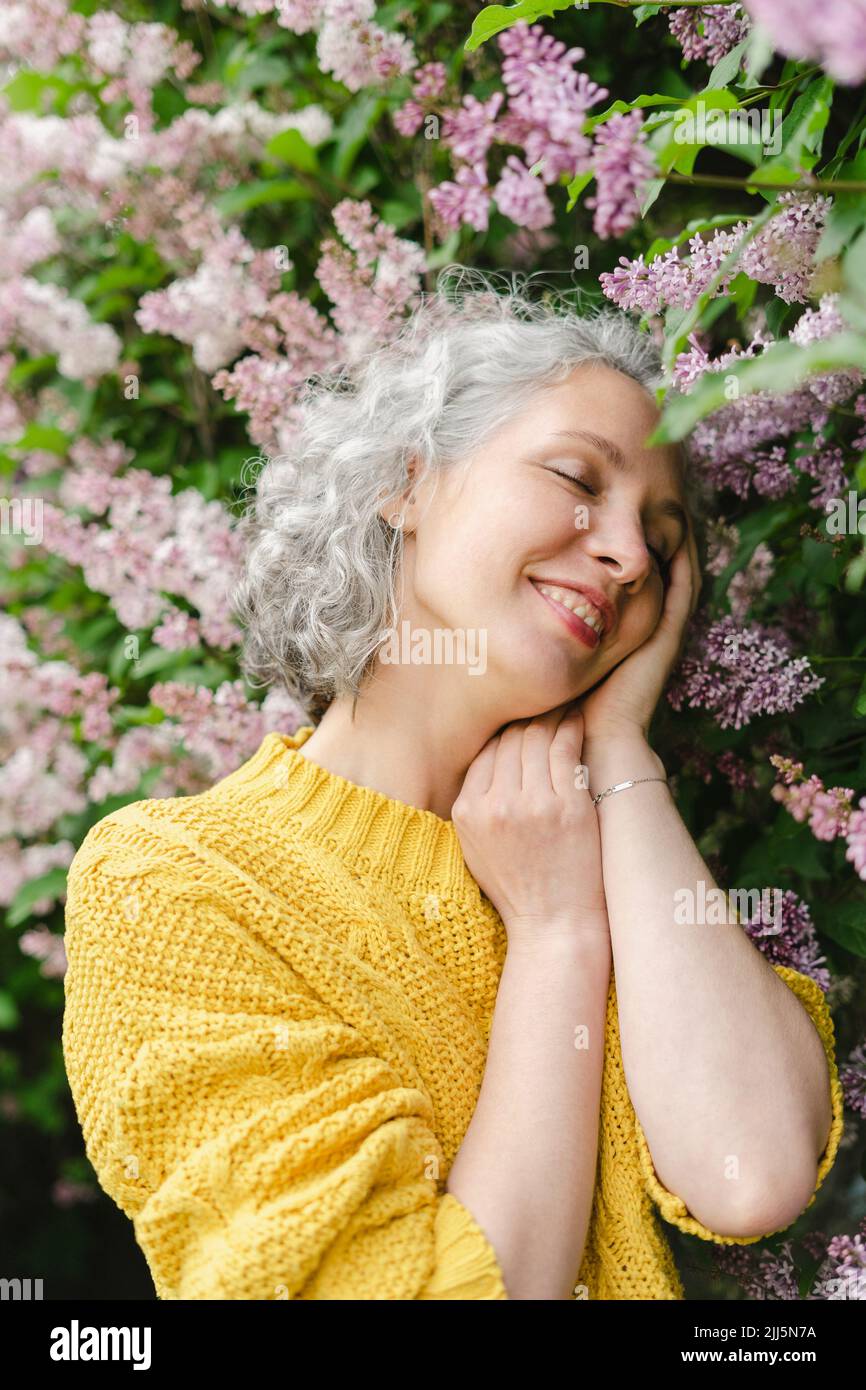 Smiling woman with eyes closed standing by lilac tree Stock Photo
