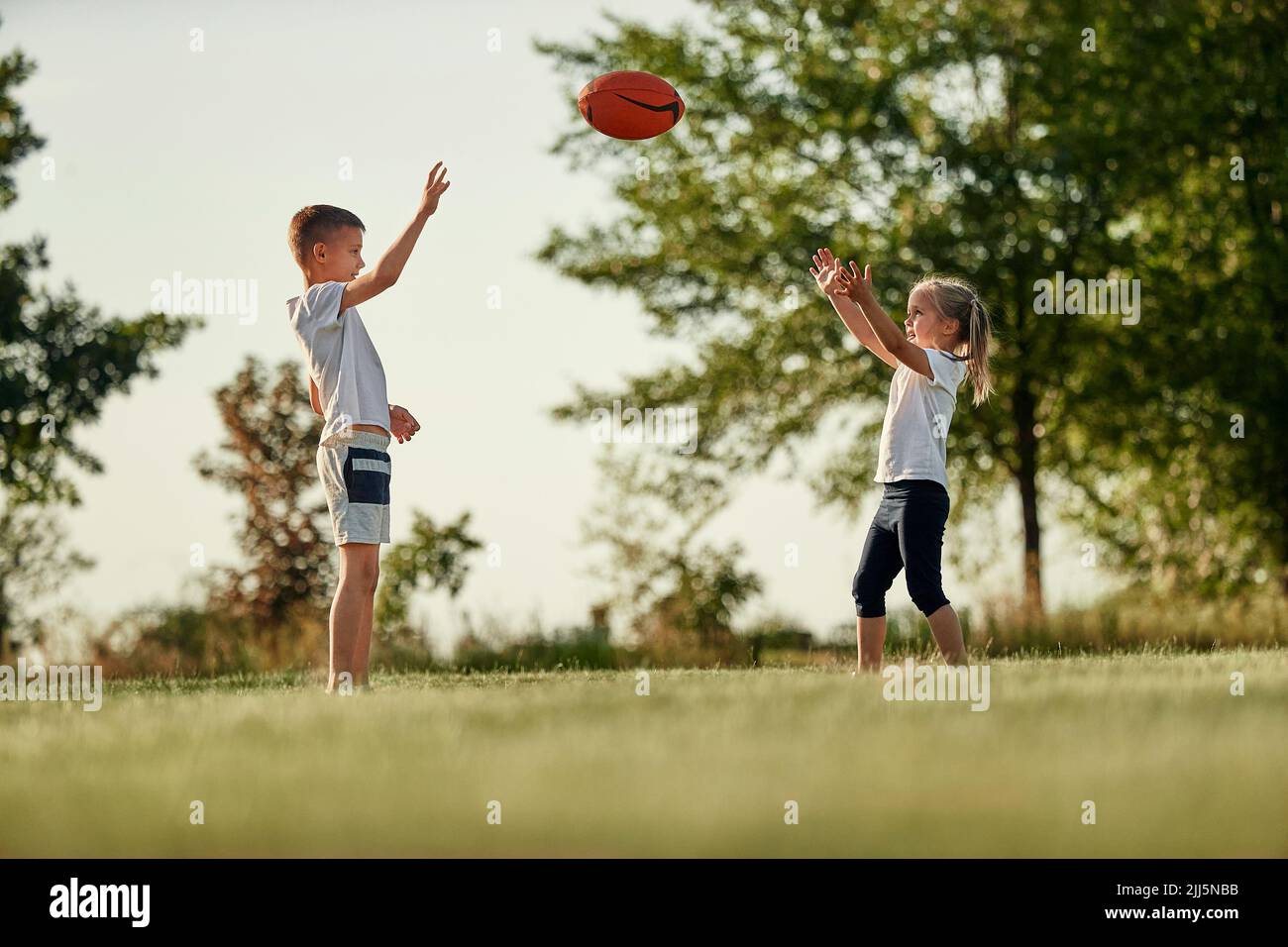 Brother and sister throwing rugby ball standing at sports field Stock Photo