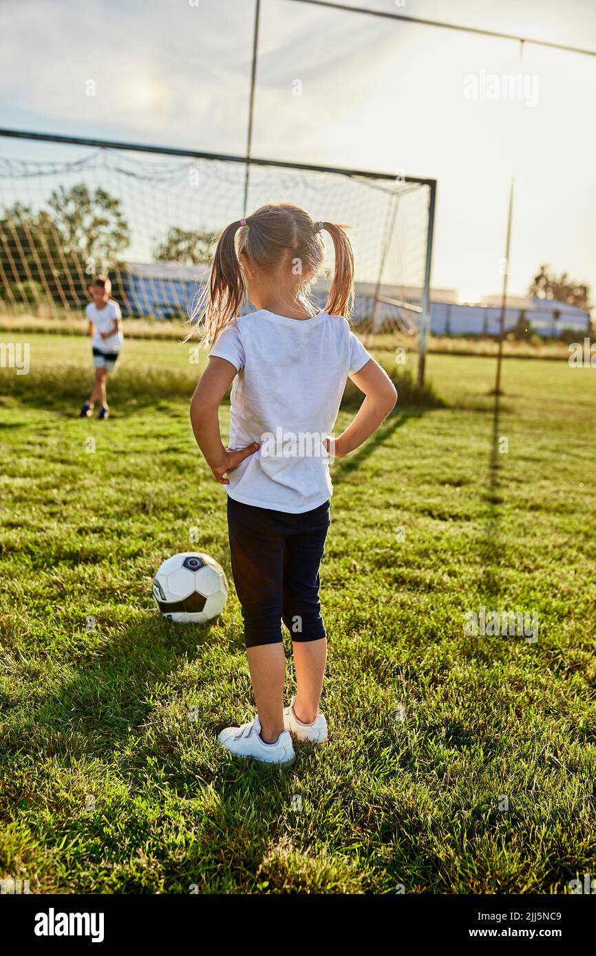 Girl standing with hand on hip in front of brother at sports field ...