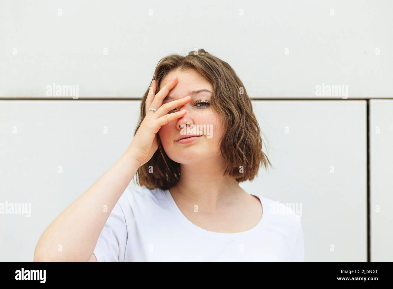 Teenage girl with brown hair covering eye in front of wall Stock Photo