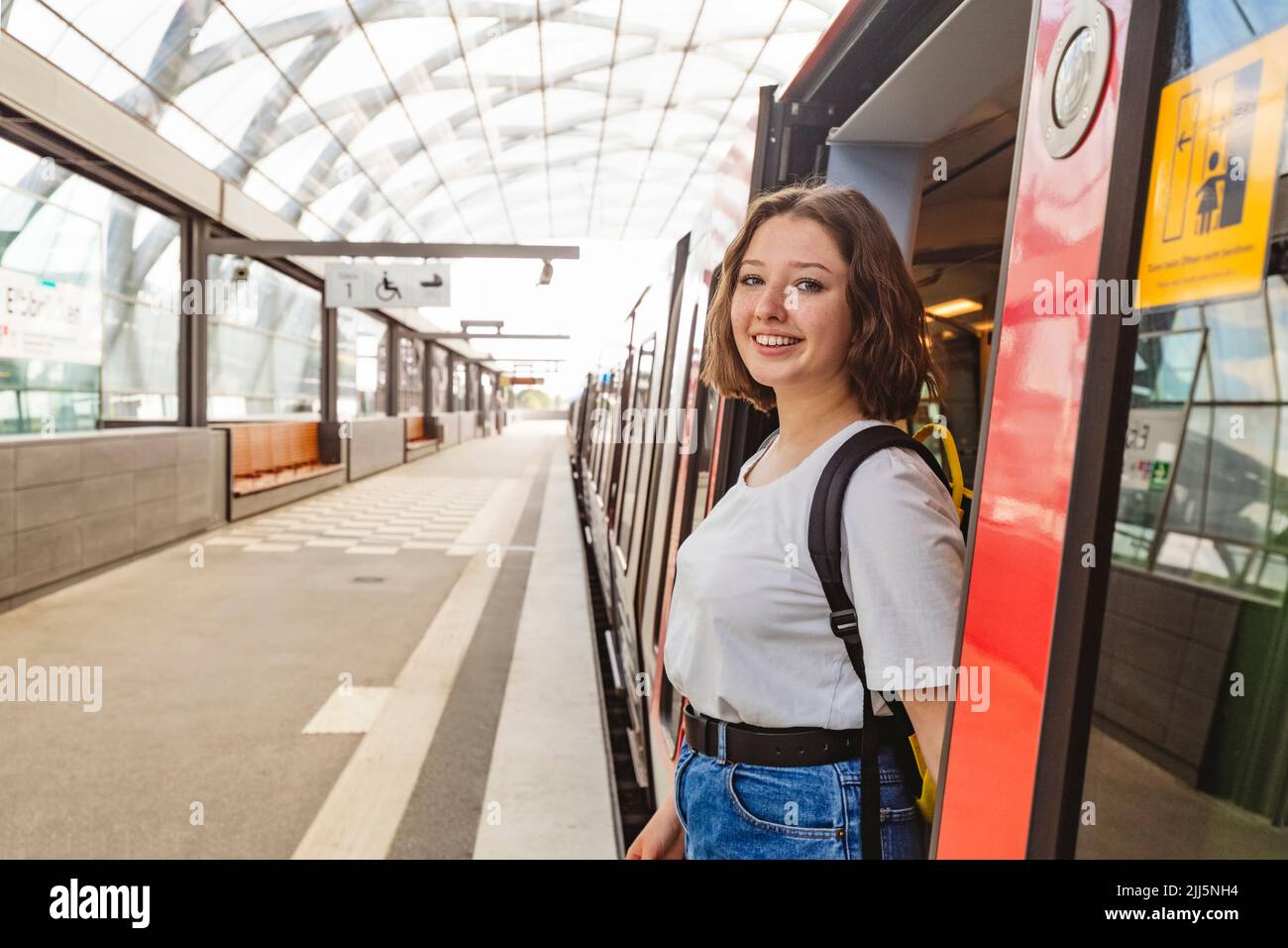 Smiling teenage girl standing at doorway of train at railroad station Stock Photo