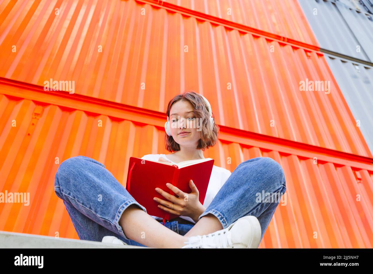 Teenage girl wearing wireless headphones writing in red notebook Stock Photo