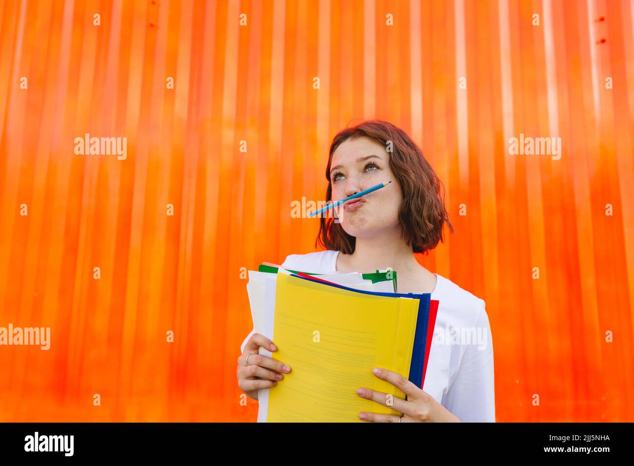 Teenage girl holding multi colored file folders puckering lips in front of orange cargo container Stock Photo