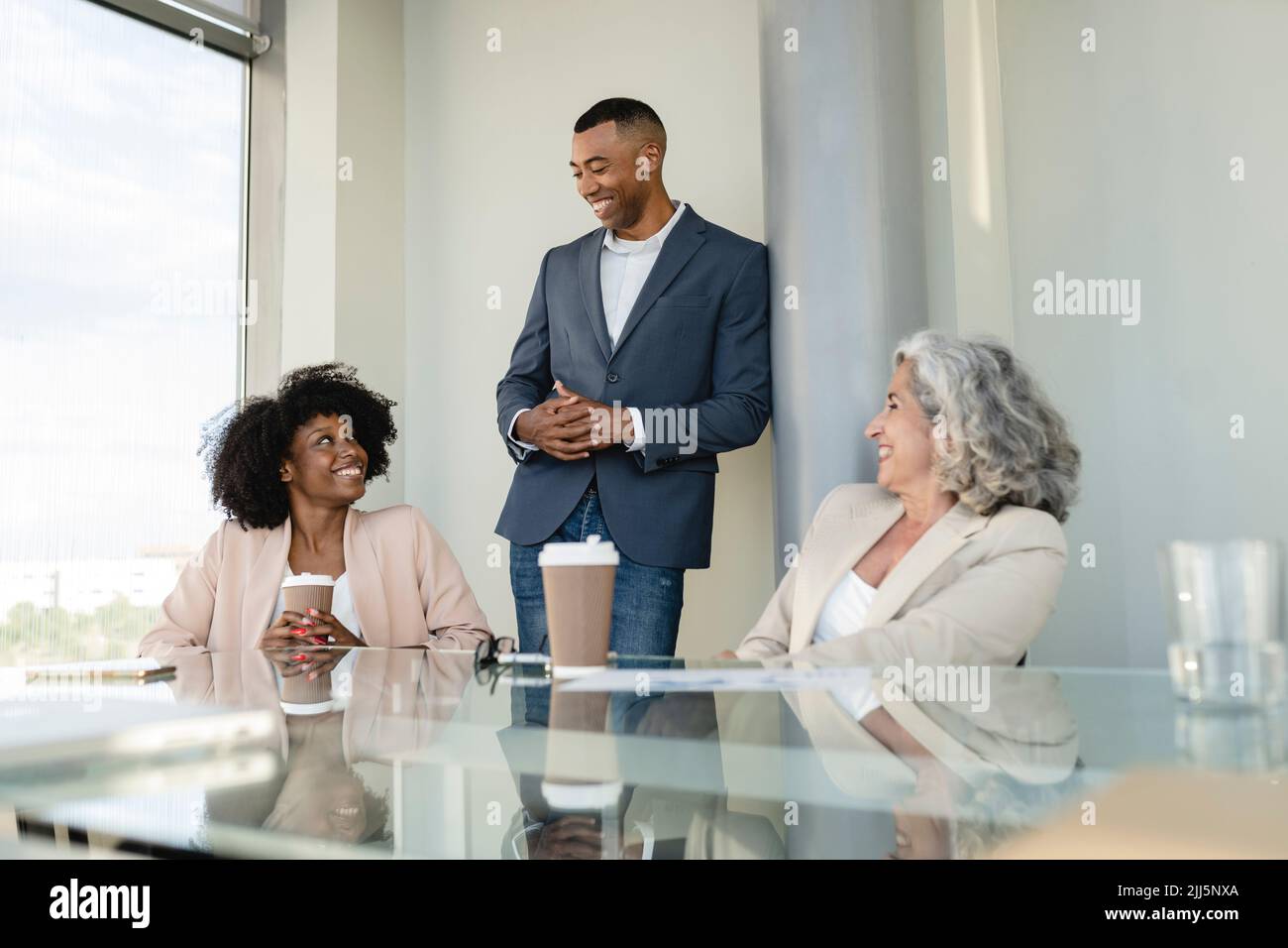 Businessman leaning on column discussing with colleagues at office Stock Photo