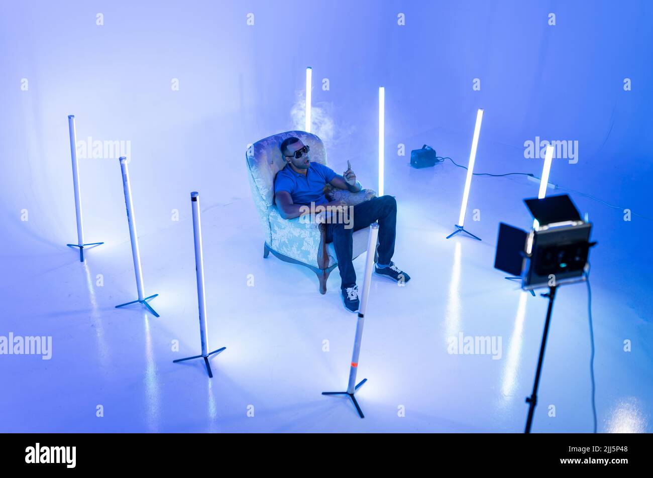Singer sitting on chair with lighting equipment in film studio Stock