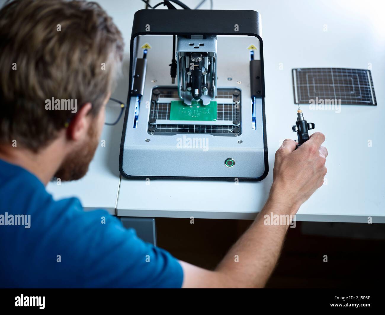 Technician looking at milling machine cutting circuit board in electronic laboratory Stock Photo