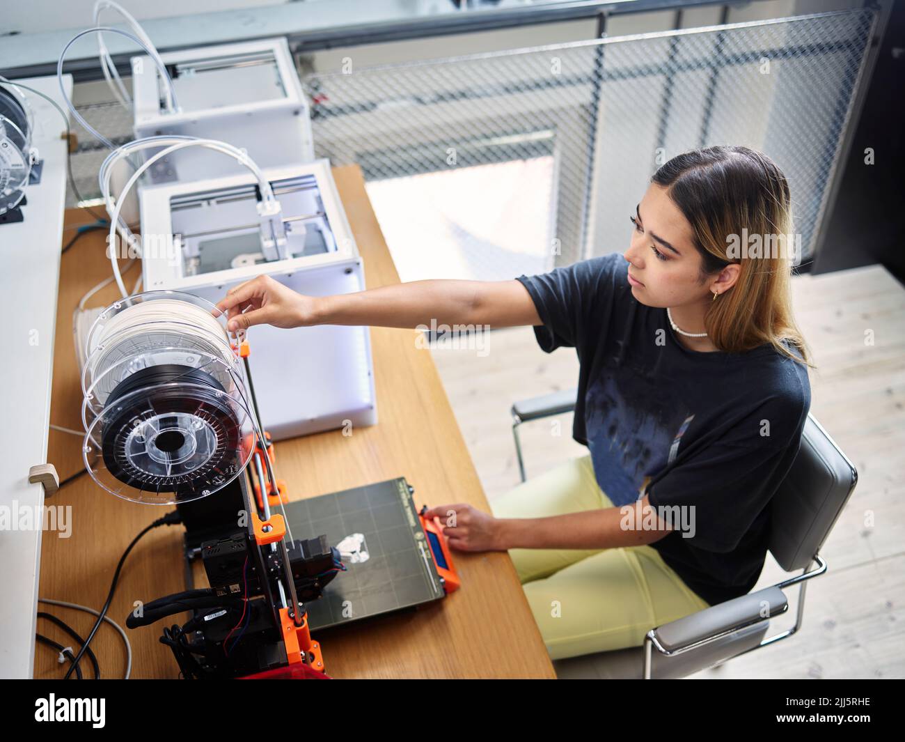 Young technician adjusting filament roll on 3d printer at workshop Stock Photo