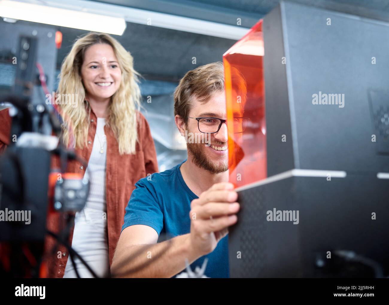 Smiling engineer assembling SLA printer with colleague at workshop Stock Photo