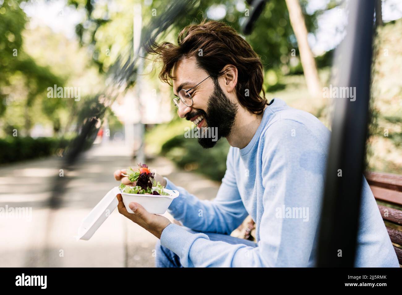 Smiling bearded man with salad sitting in park Stock Photo