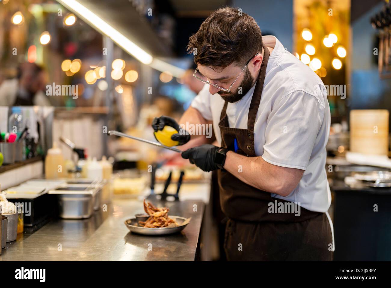 Chef wearing glove grating lemon on food in plate Stock Photo