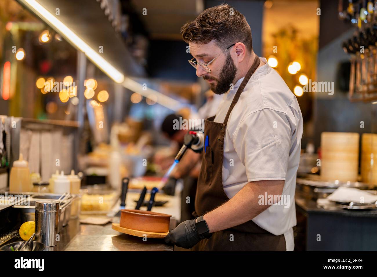 Chef using flaming torch standing at restaurant kitchen Stock Photo