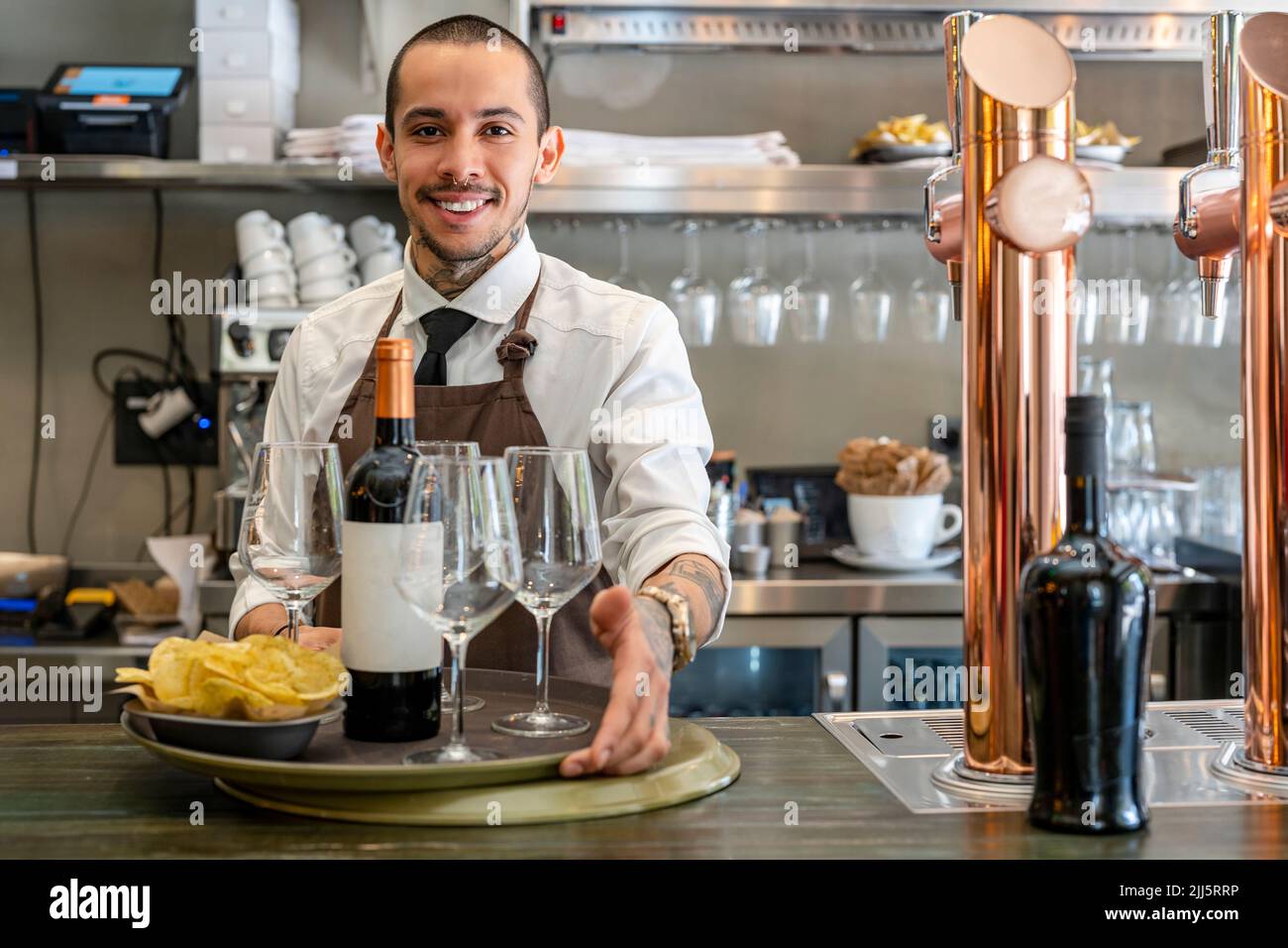 Smiling bartender with wine bottle and chips at bar counter Stock Photo
