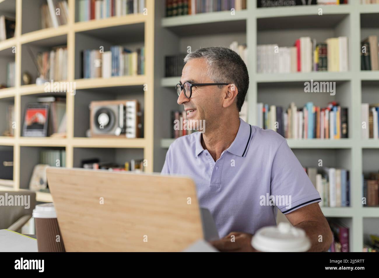 Happy mature businessman sitting in front of bookshelf Stock Photo