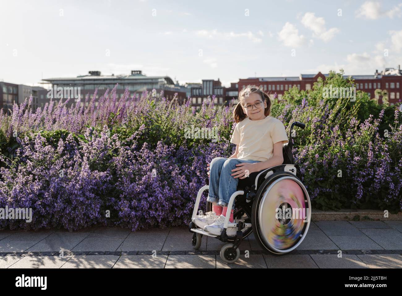 Smiling girl sitting in wheelchair in front of flowering plants Stock Photo