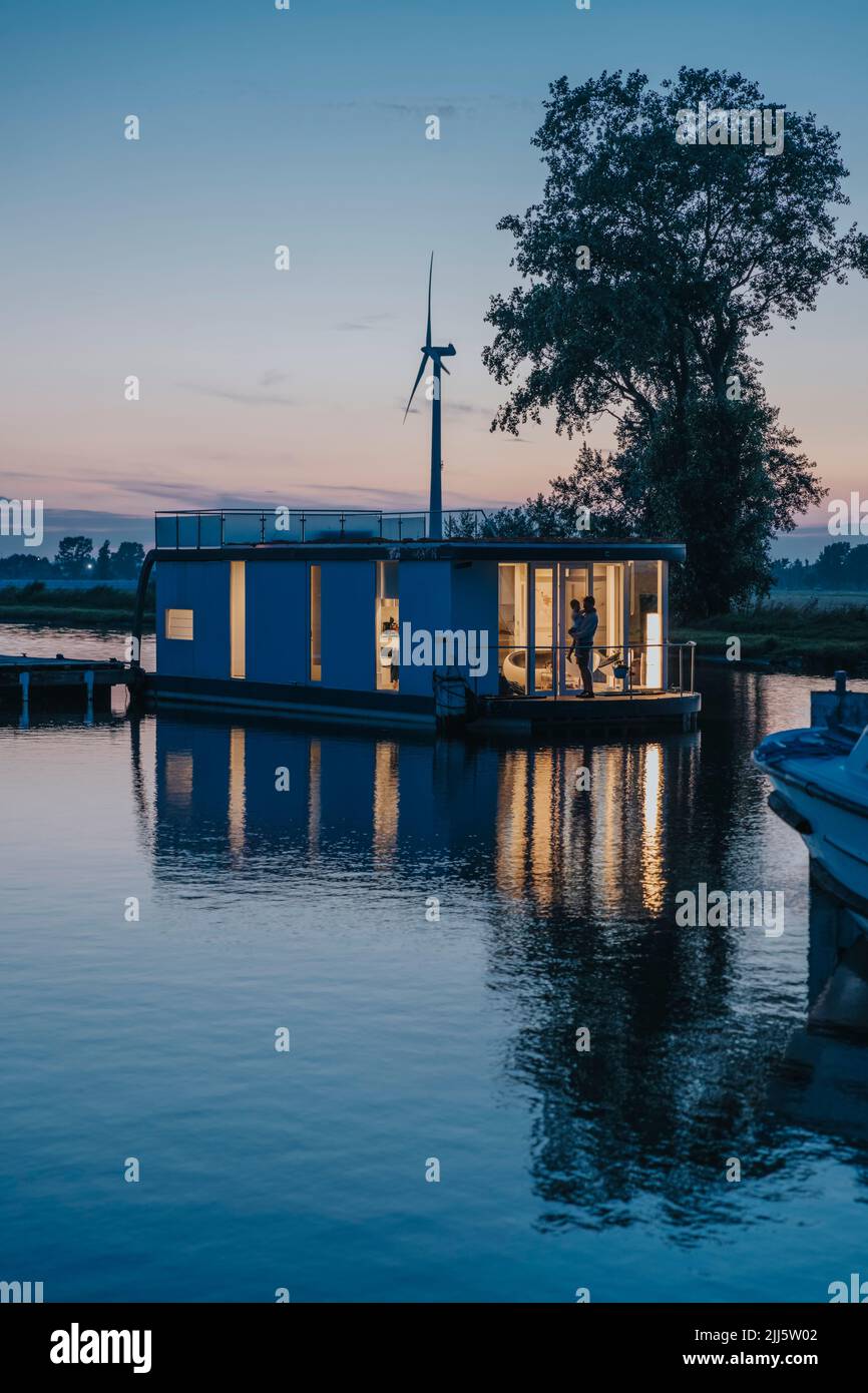 Illuminated houseboat with reflection on Yser River at sunset Stock Photo
