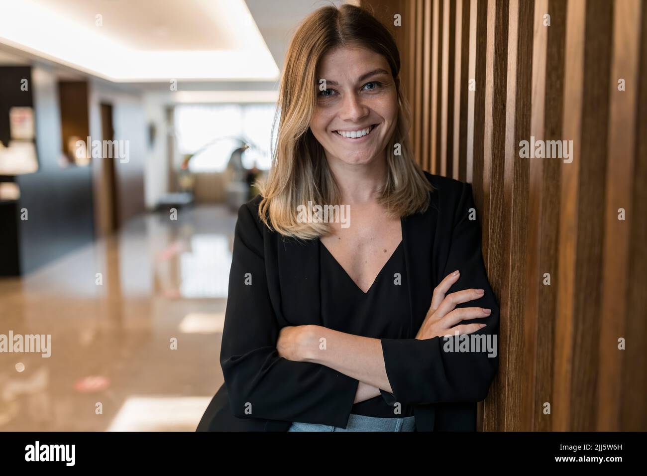 Smiling businesswoman with arms crossed standing by wooden wall at hotel Stock Photo