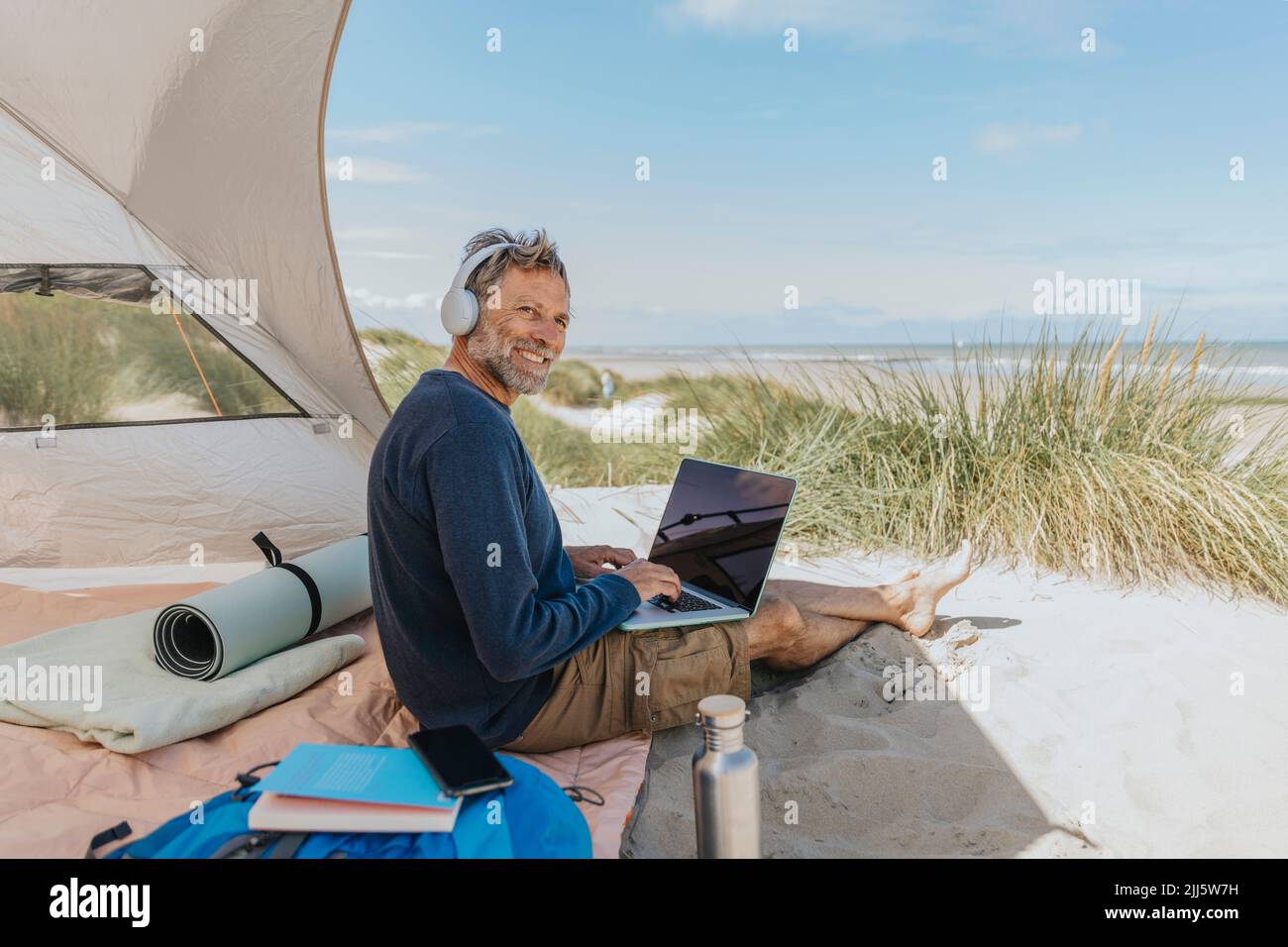 Happy freelancer wearing wireless headphones sitting at beach Stock ...