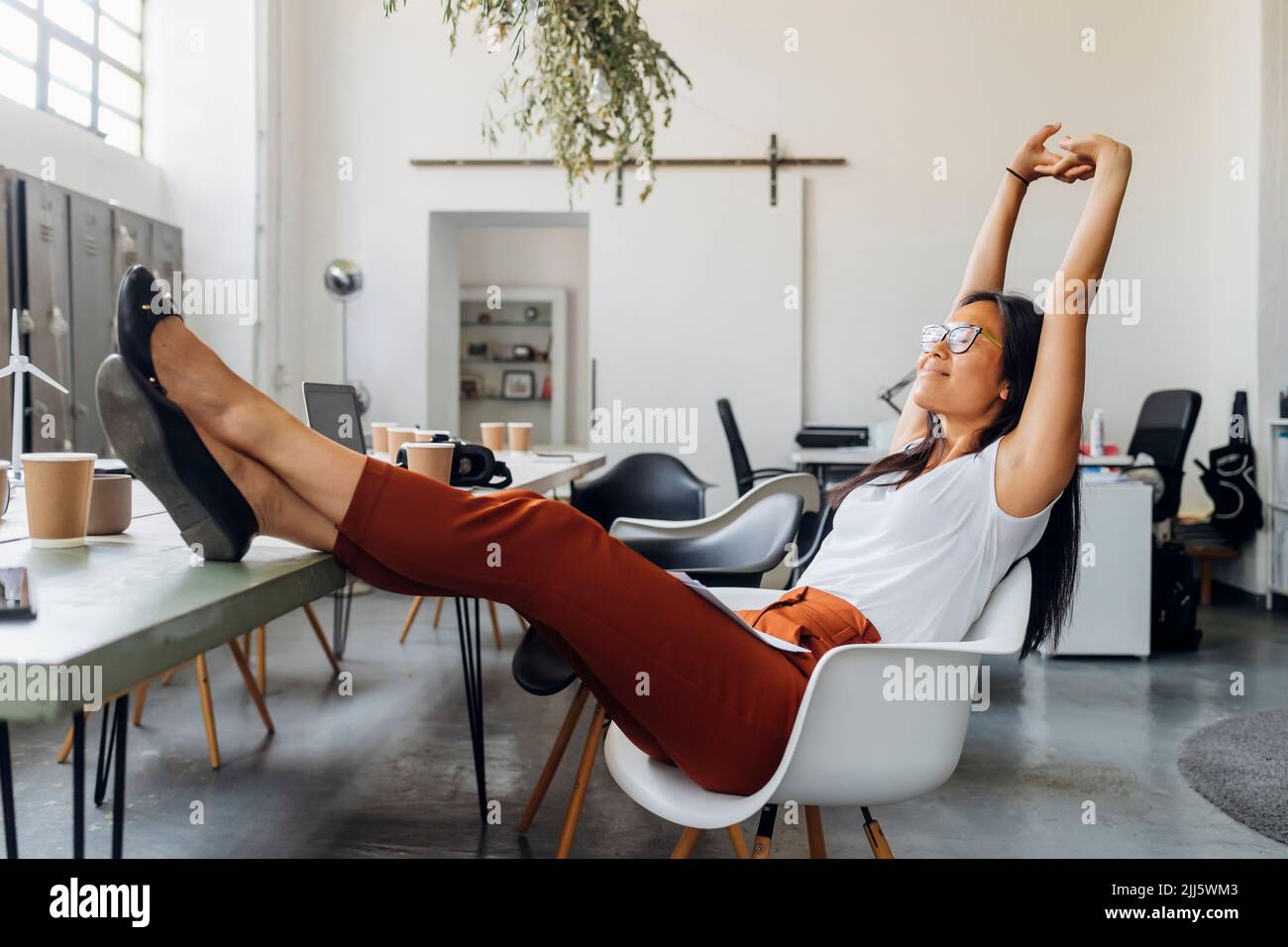 Smiling businesswoman stretching arms on chair at workplace Stock Photo