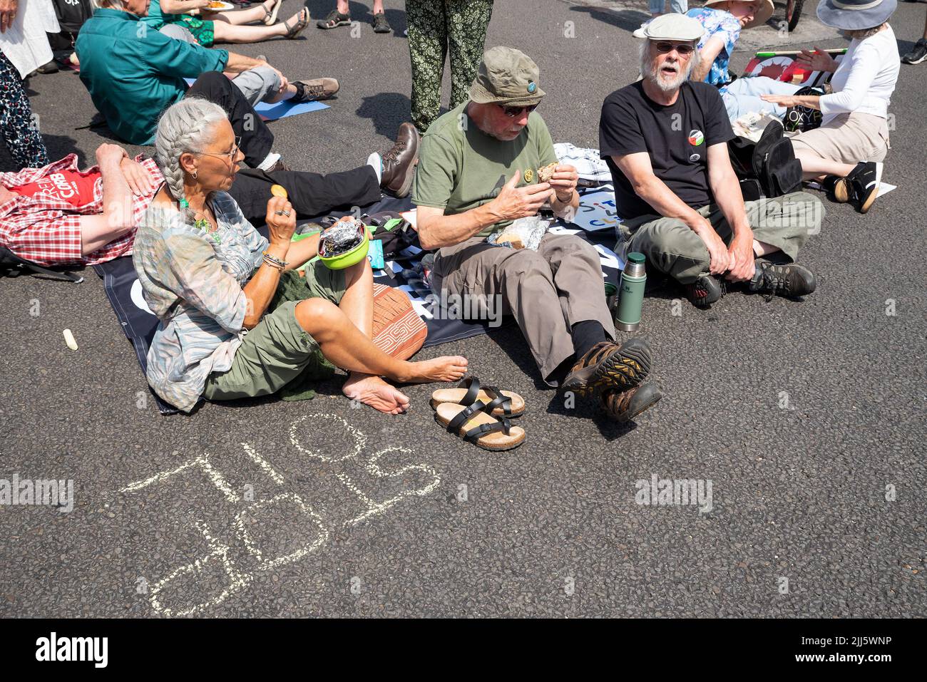 London, UK. 23rd July 2022. We All Want To Just Stop Oil Coalition: National March & Sit Down. Marchers converged upon Westminster. . Elderly protesters sit down in the road by chalked STOP OIL at parliament square and eat food. Credit: Stephen Bell/Alamy Live News Stock Photo