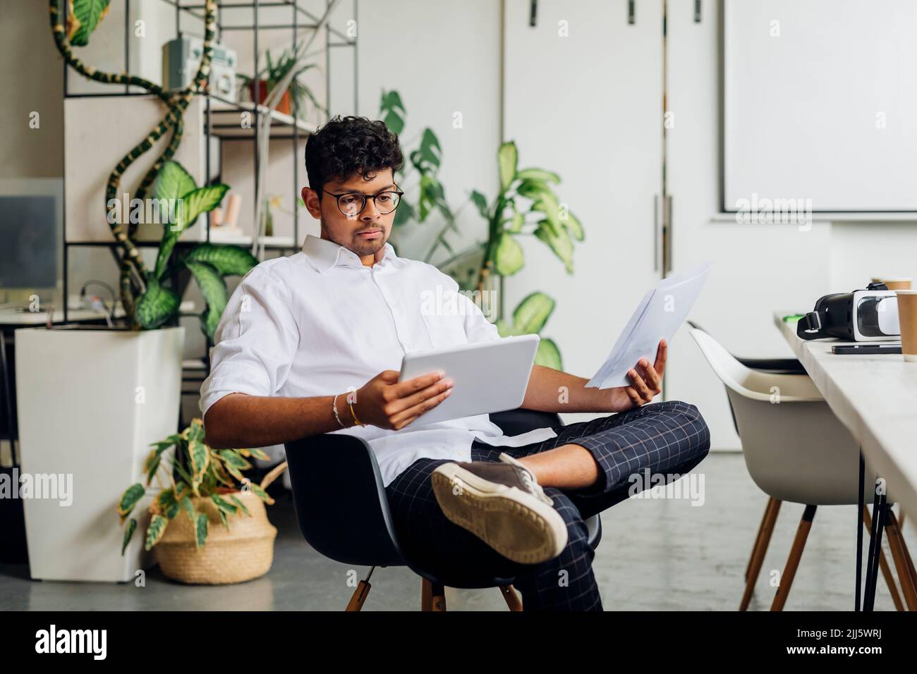 Businessman with documents using tablet PC on chair at workplace Stock Photo