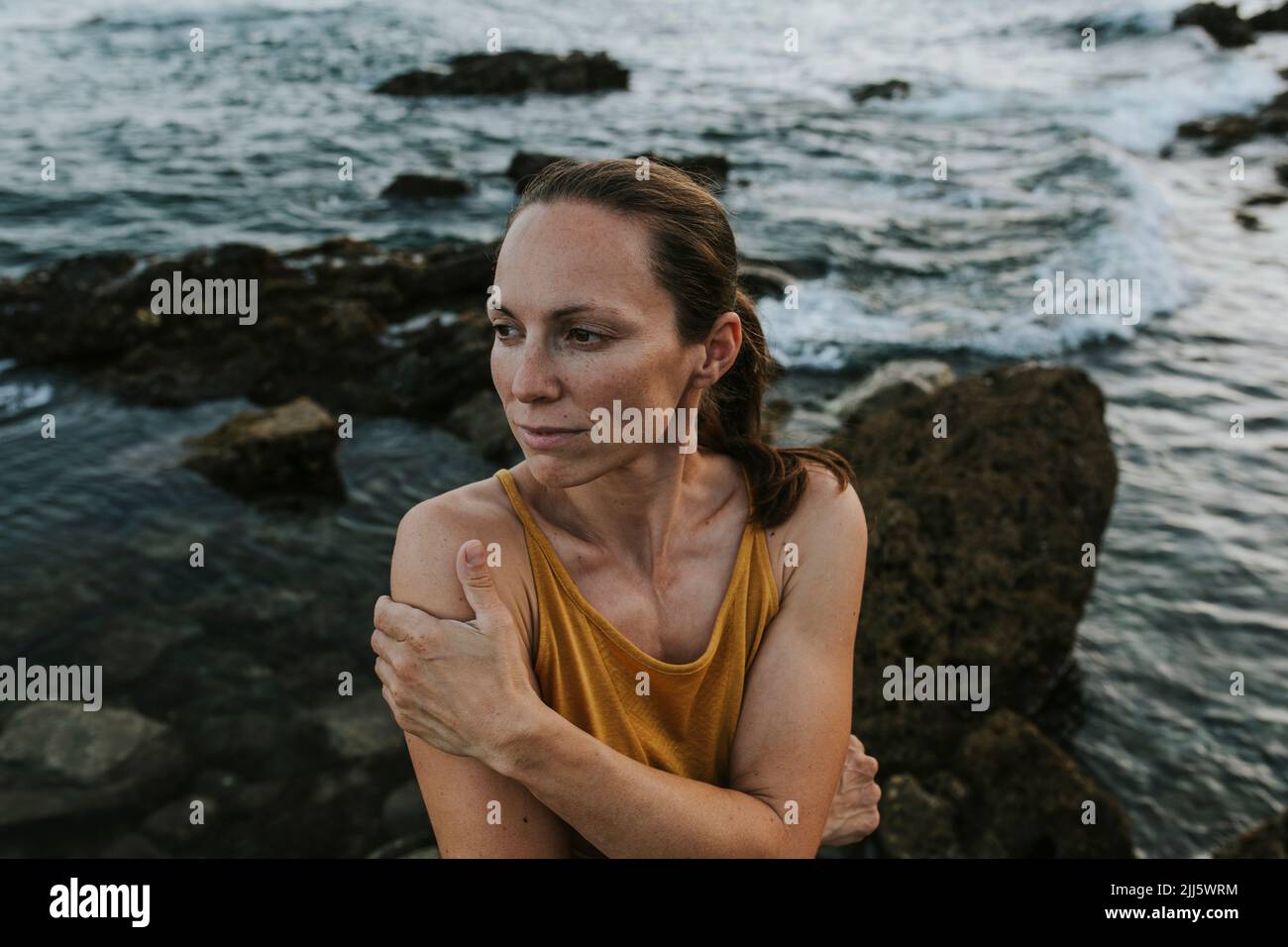 Contemplative woman hugging self at sea shore Stock Photo