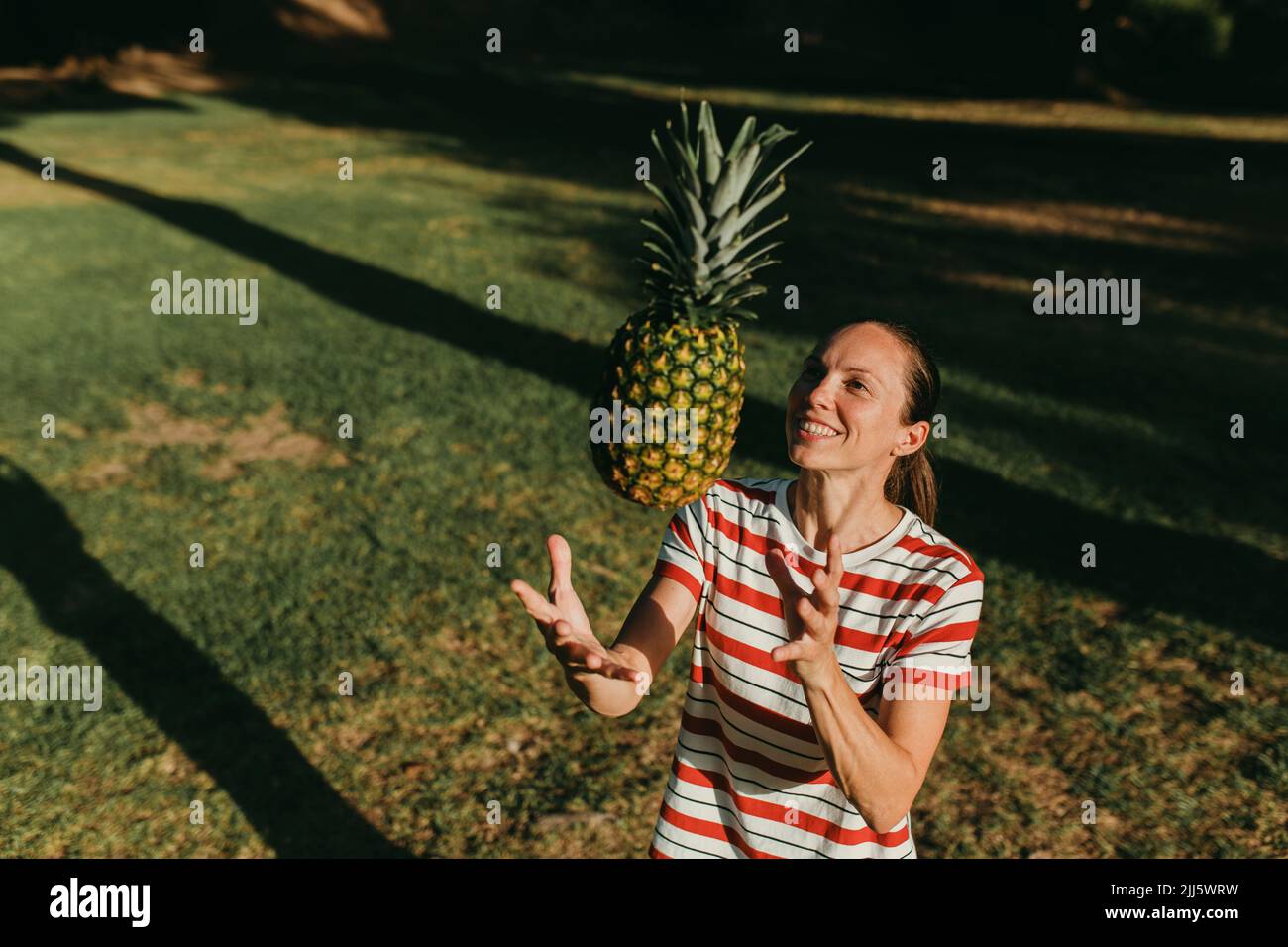 Happy woman playing with pineapple in park on sunny day Stock Photo