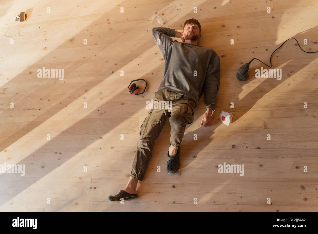 Man lying on the fresh sanded wooden floor after work. Relax under the sun in eco house Stock Photo
