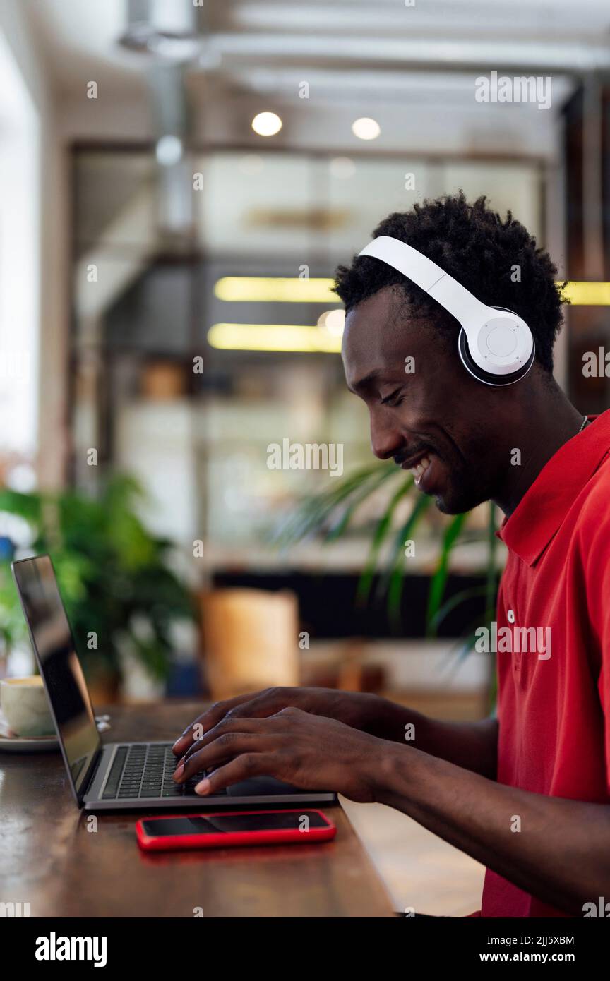Smiling man wearing wireless headphones using laptop Stock Photo