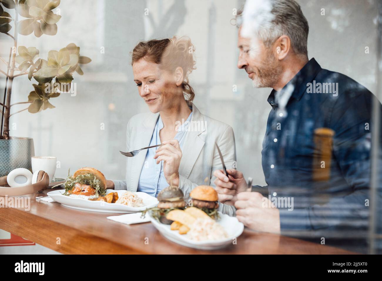 Smiling businesswoman with businessman having lunch in cafe seen through glass Stock Photo