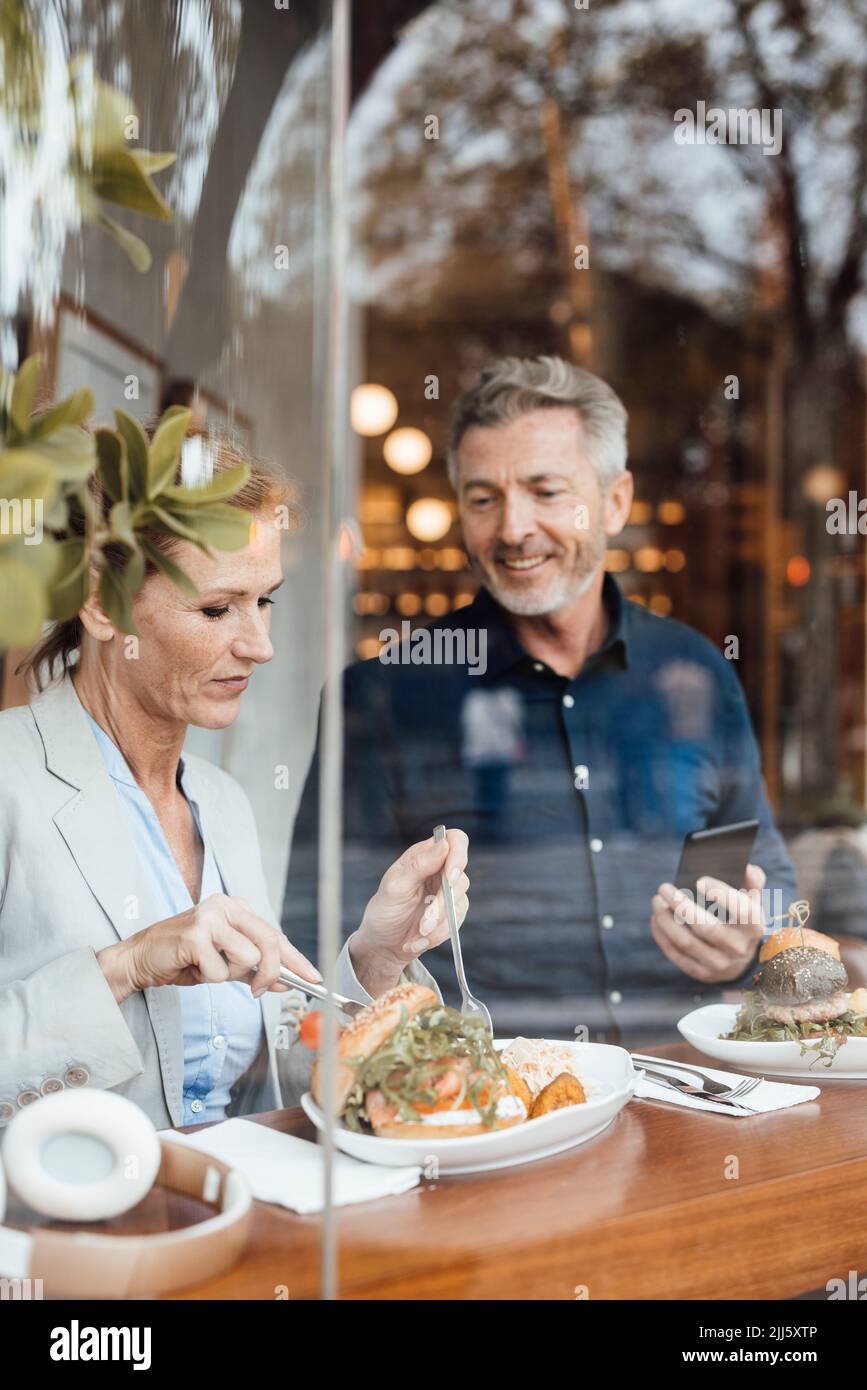 Businesswoman with businessman holding mobile phone having lunch in cafe Stock Photo